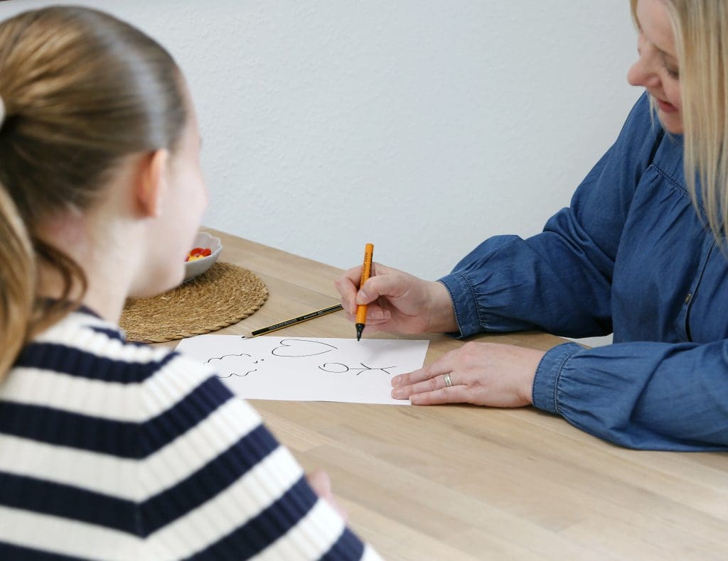 Børnepsykolog tegner mens barn kigger på